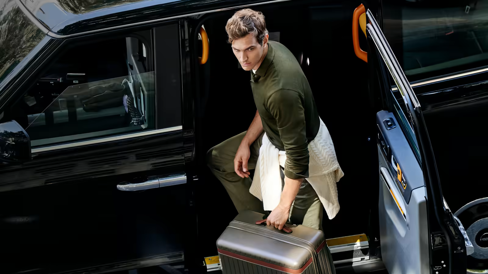 Man stepping out of a black car carrying a Carl Friedrik aluminium suitcase