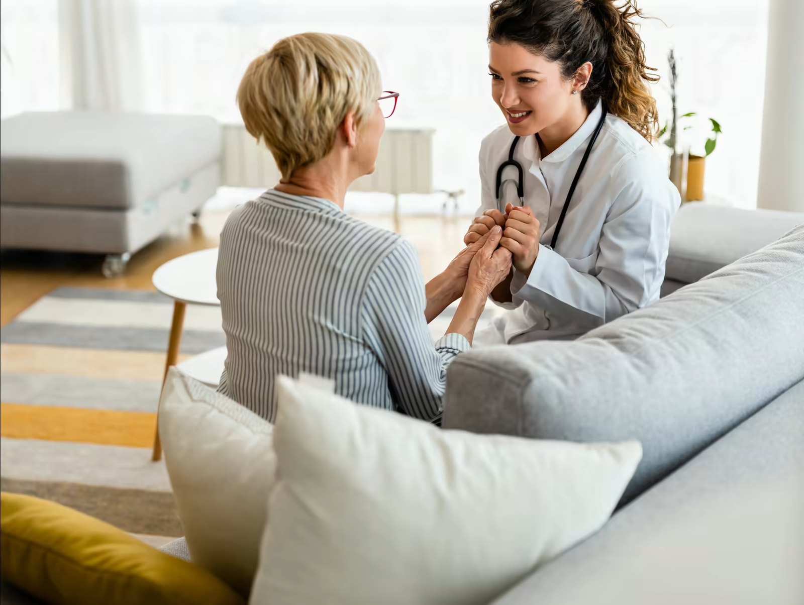 Doctor holding the hands of an older patient on a sofa