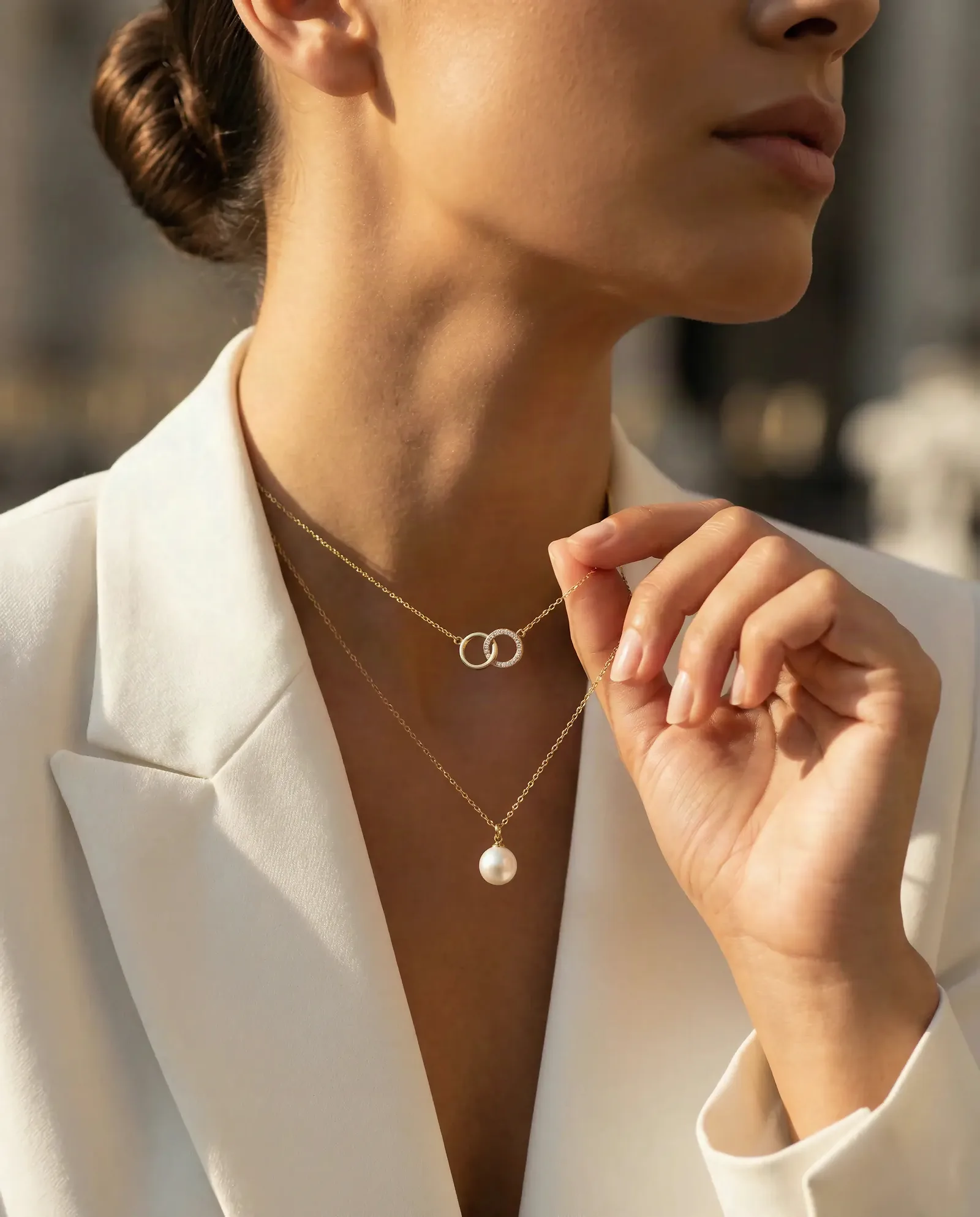 Woman in a white blazer touching layered necklaces with a pearl pendant