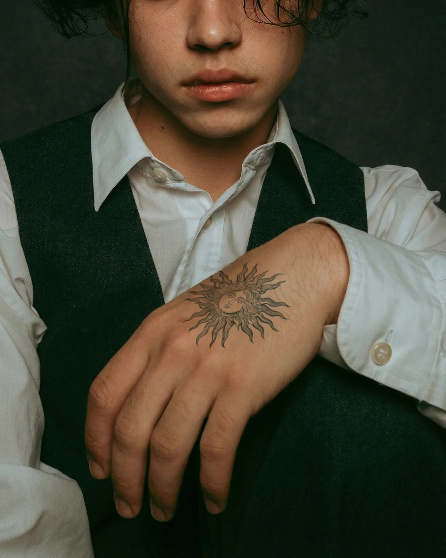Sun tattoo on the back of a hand, worn with a vest and white shirt